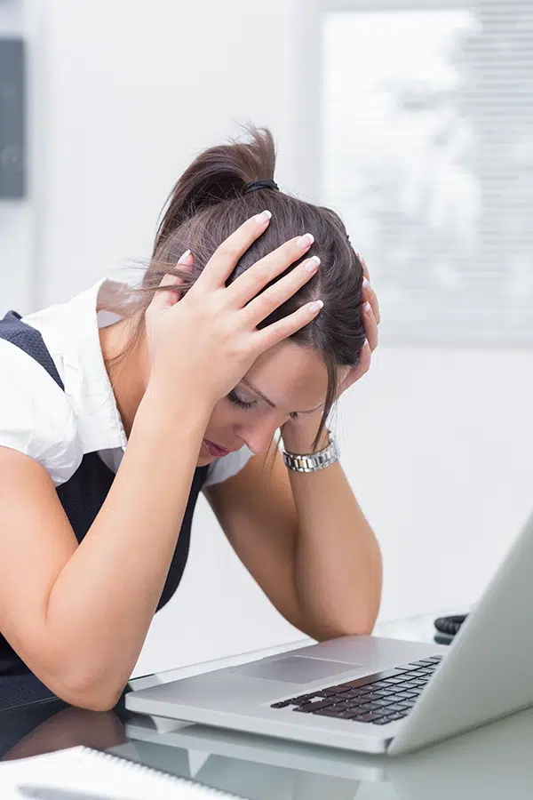 frustrated business woman sitting at her desk in front of computer with her head in her hands